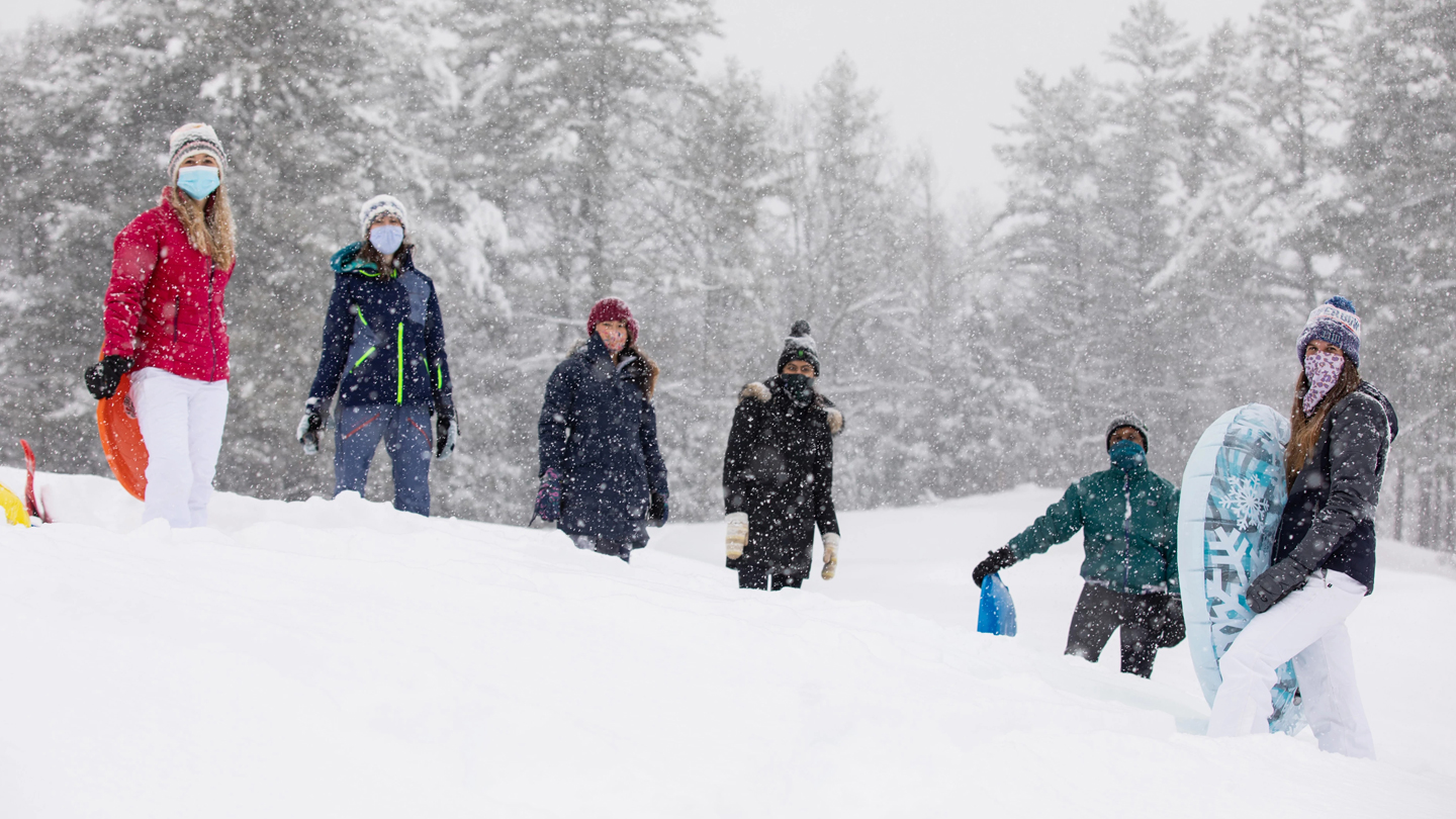 A photo of a group of students standing in snow with sleds and snow clothes on
