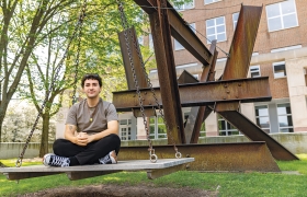 A photo of Batuhan Sarideded '26 sitting on X-Delta, a public sculpture outside Baker-Berry Library