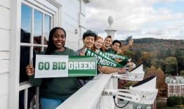 A photo of multiple students standing on the ledge of Baker Tower with Dartmouth pennants and banners