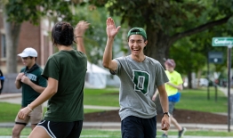 A photo of a student in a Dartmouth shirt high-fiving another student outside on campus