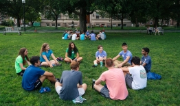 A photo of students sitting in a circle on the Green, talking
