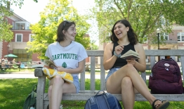 A photo of two students sitting on a bench chatting while looking at books