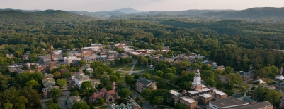 A photo of campus, taken by a drone, showing the Green, surrounding buildings, and mountains in the distance, during the summer