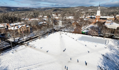 A photo of the Dartmouth Green in winter with students walking on pathways, with ice skate rink at far end, taken by a drone