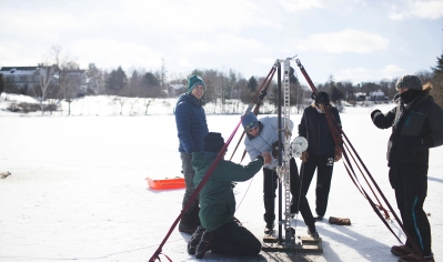 A photo of students cranking the manual drill to bring up a sample during a Quaternary Paleoclimatology class, where they drilled for ice core in Occom Pond.