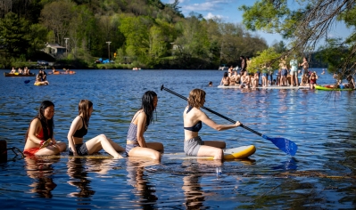 A photo of many students on the Conneticut River, with four students on a paddle board in the foreground