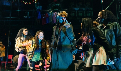 A photo of students on stage in full makeup and costumes performing RENT
