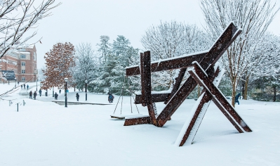 A photo of students on campus behind the sculpture X-Delta in a snowstorm
