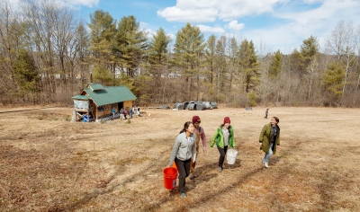 A photo of students carrying buckets of sap in front of the Dartmouth Sugar Shack