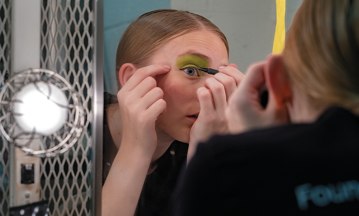A photo of a member of the Pippin cast applying makeup in a mirror