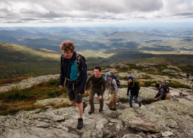 A photo of multiple students hiking up Mount Mansfield, with scenery and sky in the background