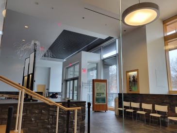 A modern lobby with high ceilings and natural lighting, featuring a reception area with artistic sculptures, a row of chairs, and a person working at a table