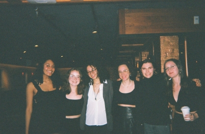 Six Dartmouth students in formal black clothing, smiling at the camera in the dark Sawtooth Kitchen