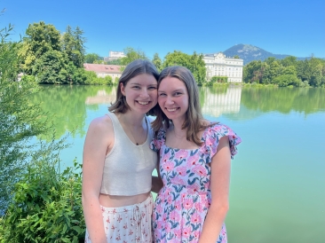 A photo of me and my sister smiling together with a lake and house in the background.