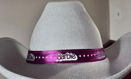 a white cowboy hat with a pink ribbon around the base that says "Barbie"