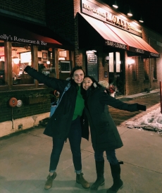 Abbi and her friend, Sarah, smile with their arms up in front of a classic, American style restaurant