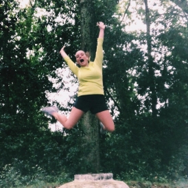 Abbi jumping in the middle of a forest in athletic gear.