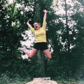 Lone pines for life! Abbi jumping in the middle of a forest in athletic gear.