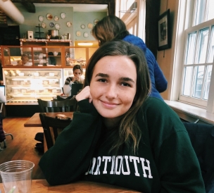 Abbi smiling at a table with the counter of Umpleby's coffee shop in the background