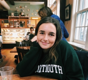 Umplebys! Abbi smiling at a table with the counter of Umpleby's coffee shop in the background
