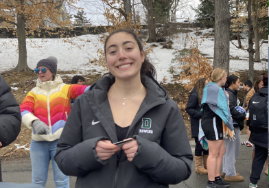 A girl with a ponytail wearing a Dartmouth rowing black jacket stands and smiles in line for Dartmouth's annual Polar Plunge tradition.
