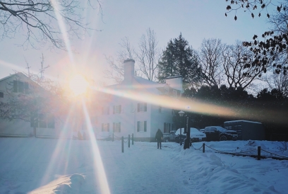 The sun rising in the background with a snowy path a white building in the foreground