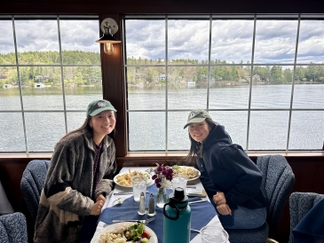 My friend and I smile for a picture before digging into our meal on the first floor of a moving ship by a window.