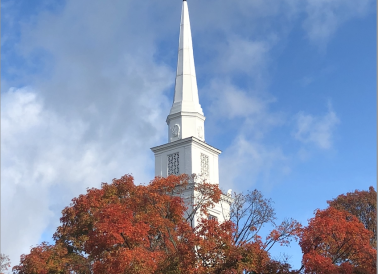 White church steeple surrounded by bright red and brown leaves 
