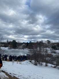 A picture of iced over Occom Pond during winter term with students who participated in the polar plunge surrounding it.