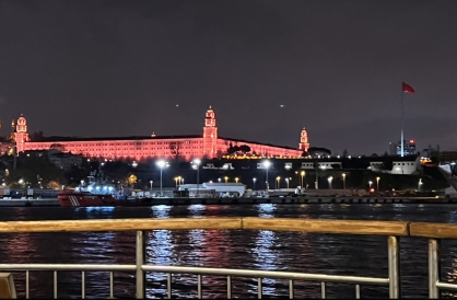 Istanbul Skyline at night from the Bosphorus, red light cast on a castle on the shore