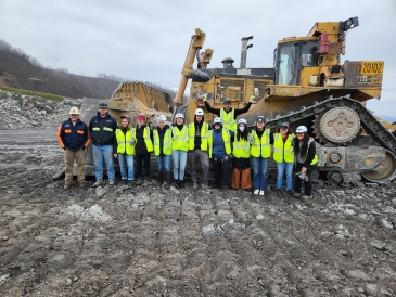 Group of students wearing constructions vests in front of large excavator at coal site