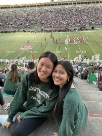 Two girls wearing Dartmouth green colors smiling in front of Harvard football stadium. 