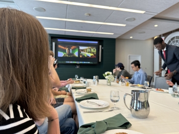 Magnuson cohort sitting down a table looking at the Zoom call on the TV