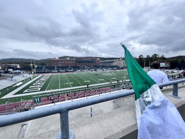 Memorial Field, a football field at Dartmouth College, during a game, as seen from the marching band's location behind a color guard flag in the home stands. 