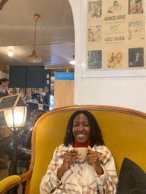 A picture of me with my eyes closed and grinning as I hold a tea mug in a cafe.