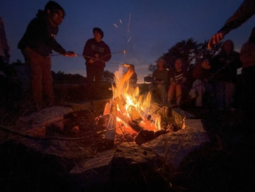 Campfire in the dark with people around it.