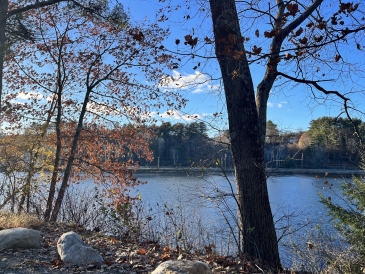 A photo of the Connecticut River from the bank. There are rocks and trees in the foreground.