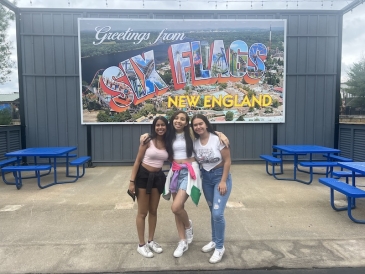 An image of three students in front of a sign board that reads Six Flags New England.