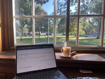 An image of a laptop, a tea cup and biscuits inside a library overlooking the Green at Dartmouth College