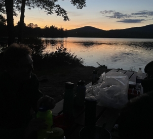 A gorgeous sunset over a lake as food lays on a table.