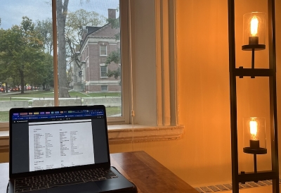 An image of a laptop on a study table next to a window and a lamp
