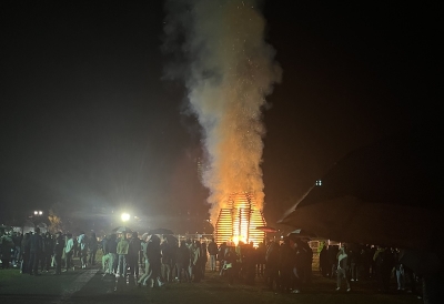 An image of a large bonfire burning against the night sky, surrounded by Dartmouth College students.