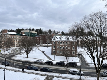 A photo of Wheeler Hall, with Fairchild and Wilder Halls in the distance. The ground is covered with snow and it is cloudy.