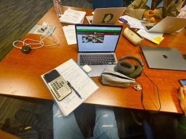 Laptops on a table filled with pencil boxes, headphones, and other stationery.