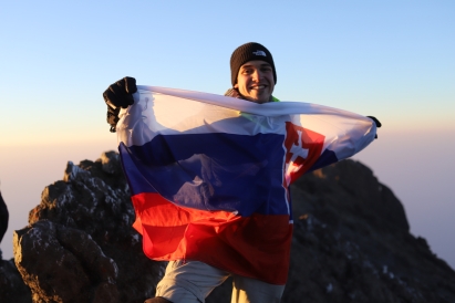 Michal standing on top of a mountain, holding the Slovak flag.