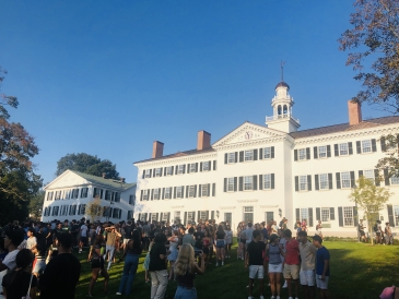 Students assemble in front of Dartmouth Hall, an angular white building with black shutters.