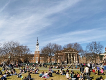 View of the Dartmouth green covered with students and Baker Berry Library in the background.