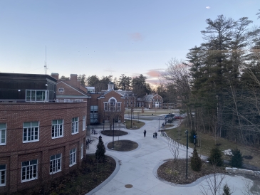 a view from the thayer school of engineering of the tuck school of business. the sun is setting and the sky is a soft pink, and student walk down below