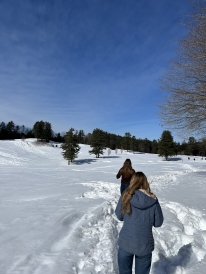 A photo of two of my friends walking in a snow-covered Pine Park. They are wearing winter clothing and walking on a narrow trail in the snow.