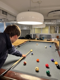 A photo of a student getting ready to take a pool shot. He is holding a cue and leaning over the table.